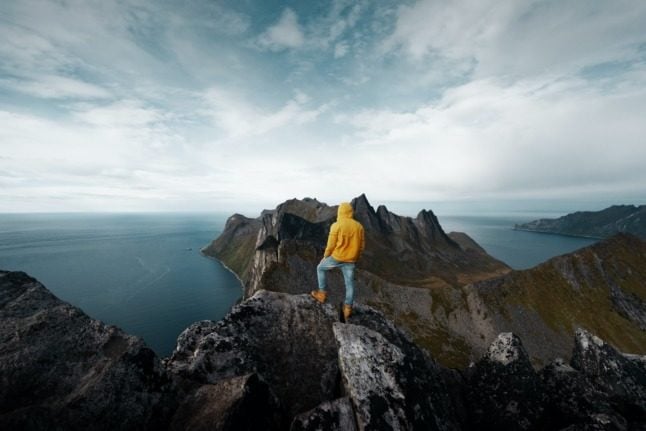 Pictured is somebody atop a mountain in Senja 