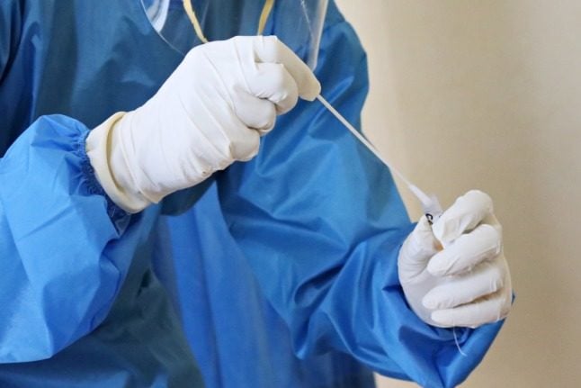 A person in PPE with a Covid-19 test swab in their hand. 